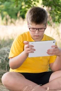 The boy in glasses looks tablet computer at nature Stock Photos
