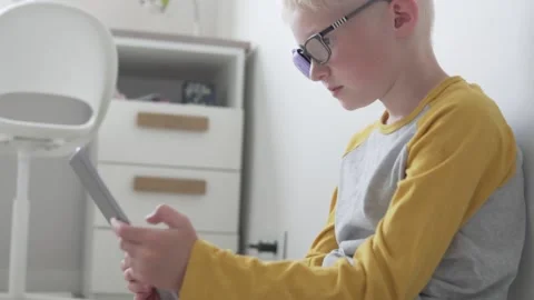 A boy with glasses with an occluder plays in a tablet at home Video stock 134587898