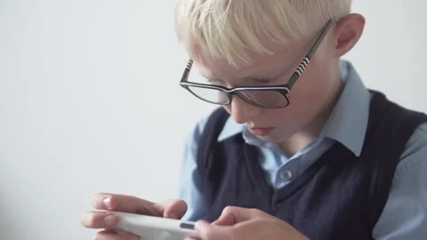 A boy with glasses plays a game on a mobile phone at school at recess Stock Footage 139608651