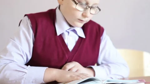Boy with glasses reading a book while sitting at a desk Stock Footage 58867022