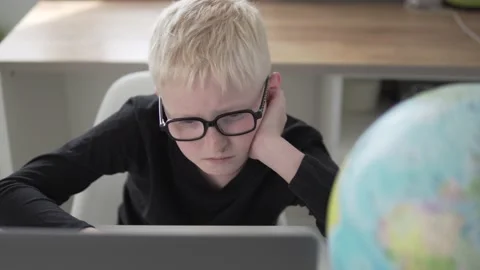 A boy with glasses sits at a desk at school and trains on a computer Stock Footage 154959106