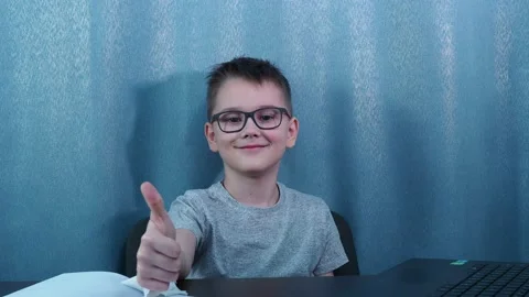 A boy with glasses sitting at a table shows a thumbs up Stock Footage 144625961