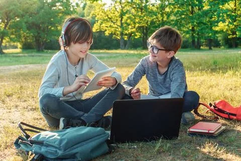 Boy in glasses smiling while looking at pupil with earphones who reading school Stock Photos
