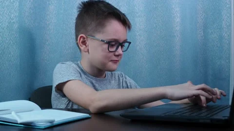 The boy with glasses types on the computer, turns and shows OK Stock Footage 144467912