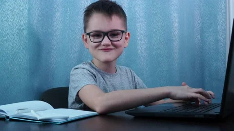 A boy with glasses types on a computer, turns around, laughs and smiles. remote Stock Footage 144683536