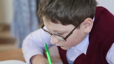 Boy with glasses writes in a notebook sitting at a desk Stock Footage 58867044