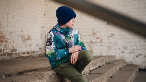 The boy goes and sits down on the concrete steps. the boy sat down to rest Stock Footage 128016555