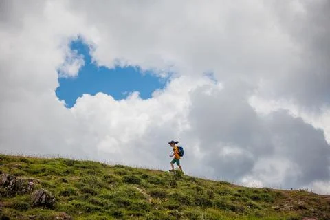 Boy goes with a backpack against the backdrop of clouds in the mountains. chi Stock Photos