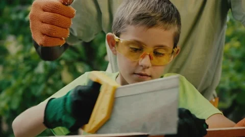 Boy in goggles and gloves cuts wooden plank with handsaw Stock Footage 198383241