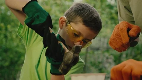 Boy in goggles hammers nail under control of carpenter Stock Footage 200774115