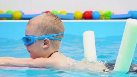 Boy in goggles learns to swim and floating, use floating items, mat in pool Stock Footage 167214334