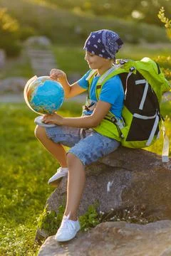 A boy in a good mood with a backpack on his shoulders examines the globe of the Stock Photos