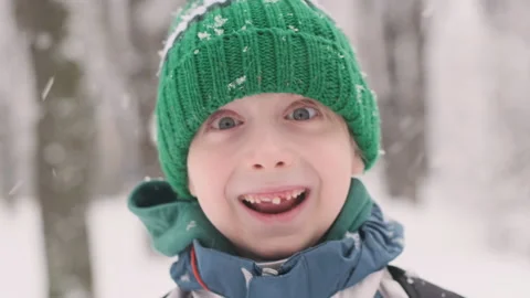 Boy in green hat on outside during snowfall looks into the camera Video stock 211688962