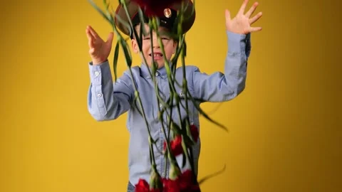 The boy in green military cap throws red flowers carnation in 9 may or 23 februa Stock Footage 147648293