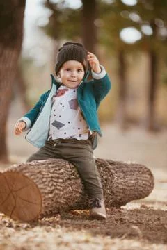 A boy in a green warm jacket and a knitted hat is sitting on a tree. He's hap Stock Photos