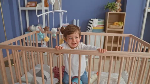 Boy gripping crib rail, reaching hand to hanging mobile in a building nurse.. Stock Footage 339256374