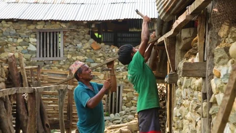Boy hammering on a wooden plank on a wallside with a man assisting him Stock Footage 77444401