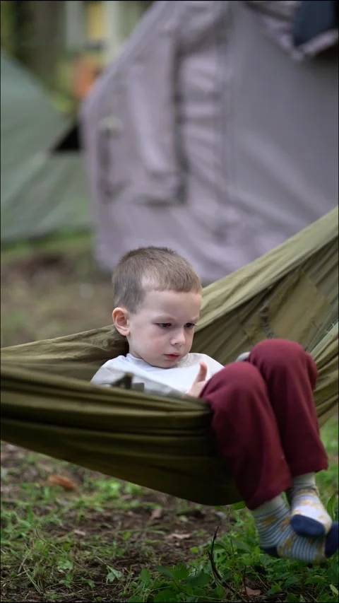 Boy in a hammock focused on his smartphone during a family camping Stock Footage 338415999