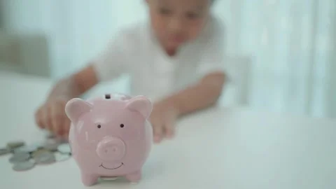 A boy hand putting coins into pink piggy bank saving money is an investment Stock Footage 265935239