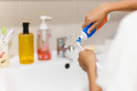 Boy hand putting toothpaste on toothbrush in the bathroom. Stock Photos
