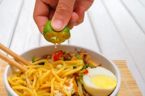 Boy hand squeezing lime on Malay Mee Rebus in the bowl  with chopsticks on wh Stock Photos