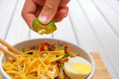 Boy hand squeezing lime on Malay Mee Rebus in the bowl  with chopsticks on wh Stock Photos