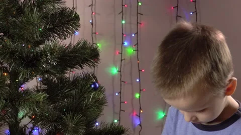 The boy hangs balls on the Christmas tree against the background of blinking Stock-Footage 143766964
