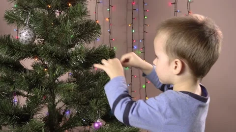 The boy hangs balls on the Christmas tree against the background of blinking 스톡 동영상 144346533