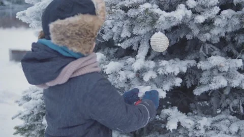 Boy hangs a red ball on a snow-covered christmas tree Stock Footage 144728042