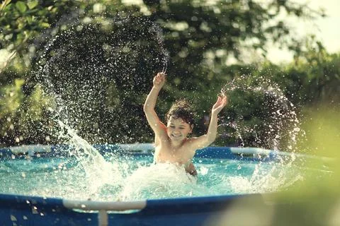 A boy happily splashes in the pool in the summer heat Stock Photos
