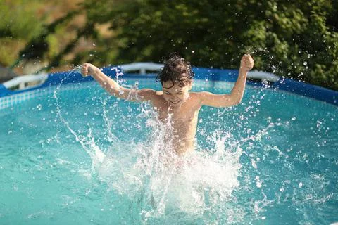 A boy happily splashes in the pool in the summer heat Stock Photos