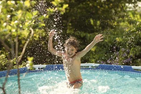 A boy happily splashes in the pool in the summer heat Stock Photos