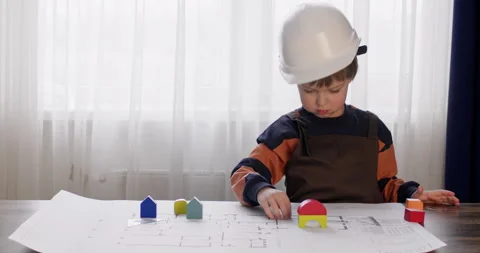 Boy in hardhat measures drawing and puts constructor cubes Vidéo 243216890