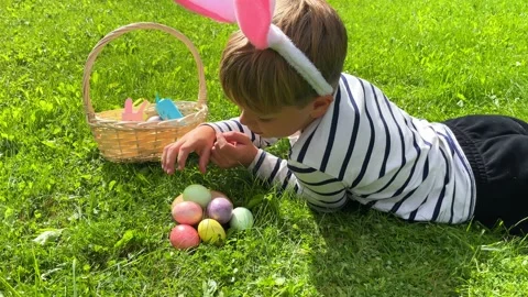 A boy with hare ears lies on the grass with colorful eggs. Stock Footage 228200723