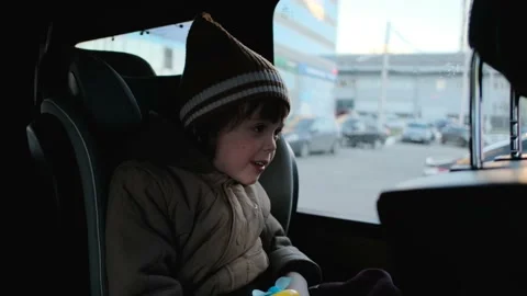 Boy in hat and jacket talks sitting in booster chair in car Stock Footage 154395380