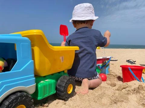 Boy with a hat playing in the sand on the beach with toys and truck Stock Photos