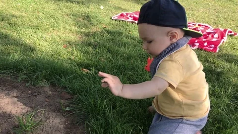 Boy with hat plays with toy and tear grass trying to stand up Video stock 112767572