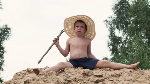 Boy in hat sitting on pile of sand. Stock Footage 287534621