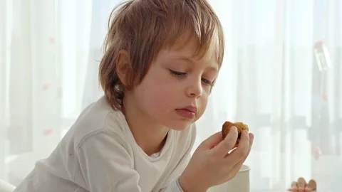 Boy have breakfast in modern kitchen. Boy eat cookie with milk. White Table in Stock Footage 103676276