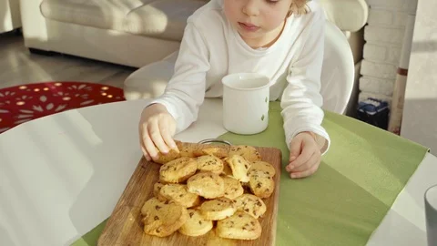 Boy have breakfast in modern kitchen. Boy eat cookie with milk. White Table in Video stock 103678276