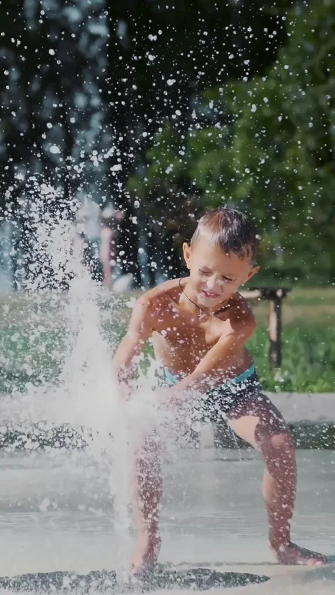 Boy having fun between water jets, in fountain, run around, sprinkle, have fun, Stock Footage 314785963
