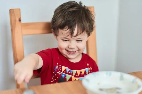 A boy is having fun at the breakfast table eating oatmeal Stock Photos