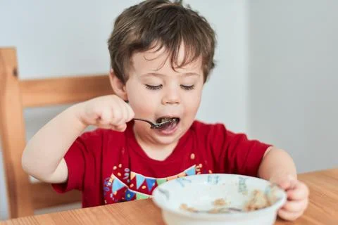 A boy is having fun at the breakfast table eating oatmeal Stock Photos