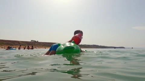 Boy having fun riding inflatable crocodile in sea water low angle Stock Footage 279426580