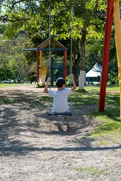 Boy having fun on a swing. Child playing on outdoor playground. Stock Photos