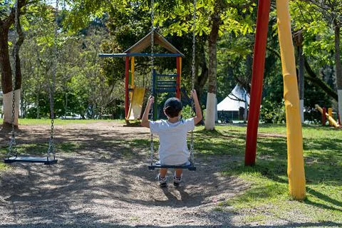 Boy having fun on a swing. Child playing on outdoor playground. Stock Photos