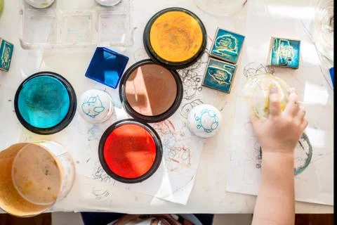 Boy is having fun while playing with stamps and tempera paints on wooden work Stock Photos