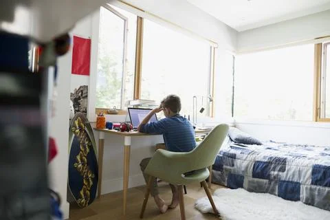 Boy with head in hands using laptop in bedroom Stock Photos