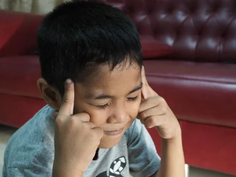 A boy in a headache On the background of the red sofa in the house. Stock Photos