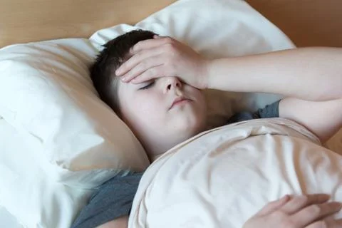 Boy with headache lying in bed Stock Photos